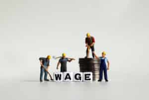 Construction men stand on coins next to the word wage, victims of unpaid work time.