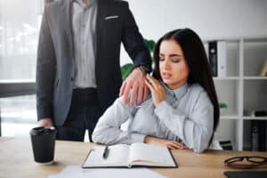 Woman tries to brush her manager's hand from her shoulder at work