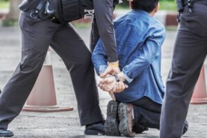 Man is on his knees on the ground being handcuffed Man on his knees being handcuffed by police after a violent altercation.