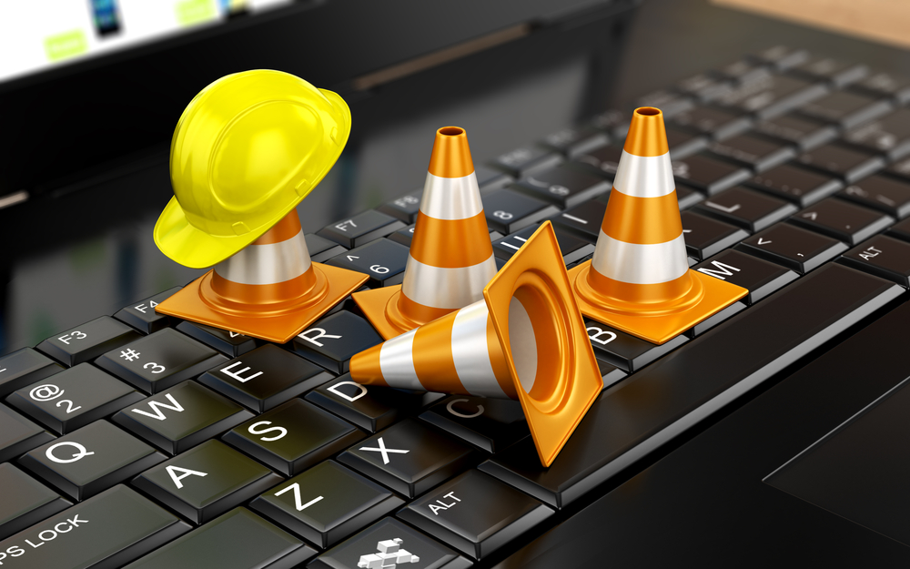 Man is on his knees on the ground being handcuffed Construction equipment on a computer keyboard representing fraud.